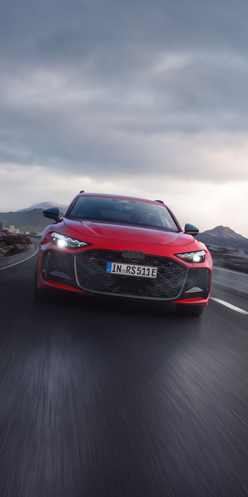 Ein roter Audi RS 5 Avant fährt auf einer Straße in einer bergigen Landschaft. Der Himmel ist bewölkt.