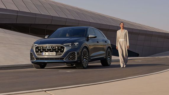 Seitliche Frontalansicht eines Audi SQ8 SUV mit einer Frau daneben